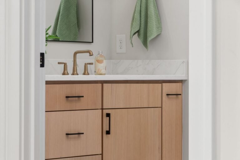 Bathroom vanity in pale wood with brass tapware and a wide mirror reflecting daylight