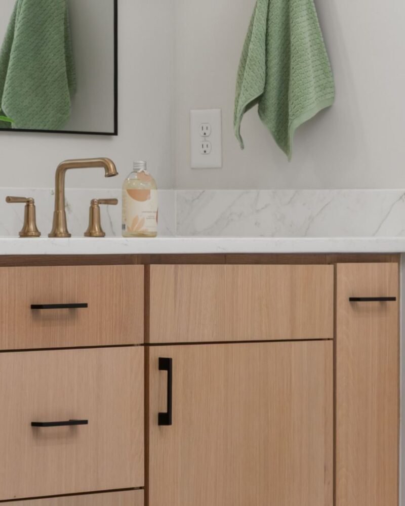 Bathroom vanity in pale wood with brass tapware and a wide mirror reflecting daylight