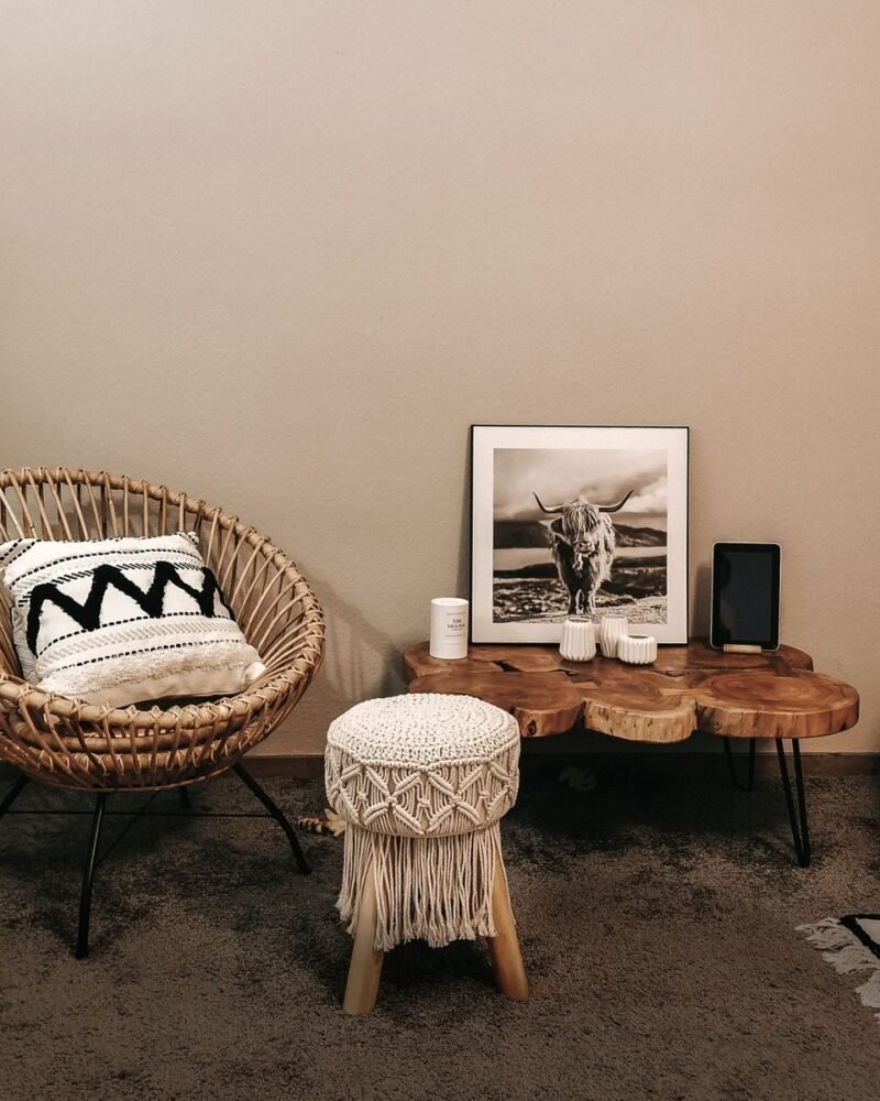 Bohemian living room with a woven wicker armchair, a macrame stool and layered textiles against a pale wall