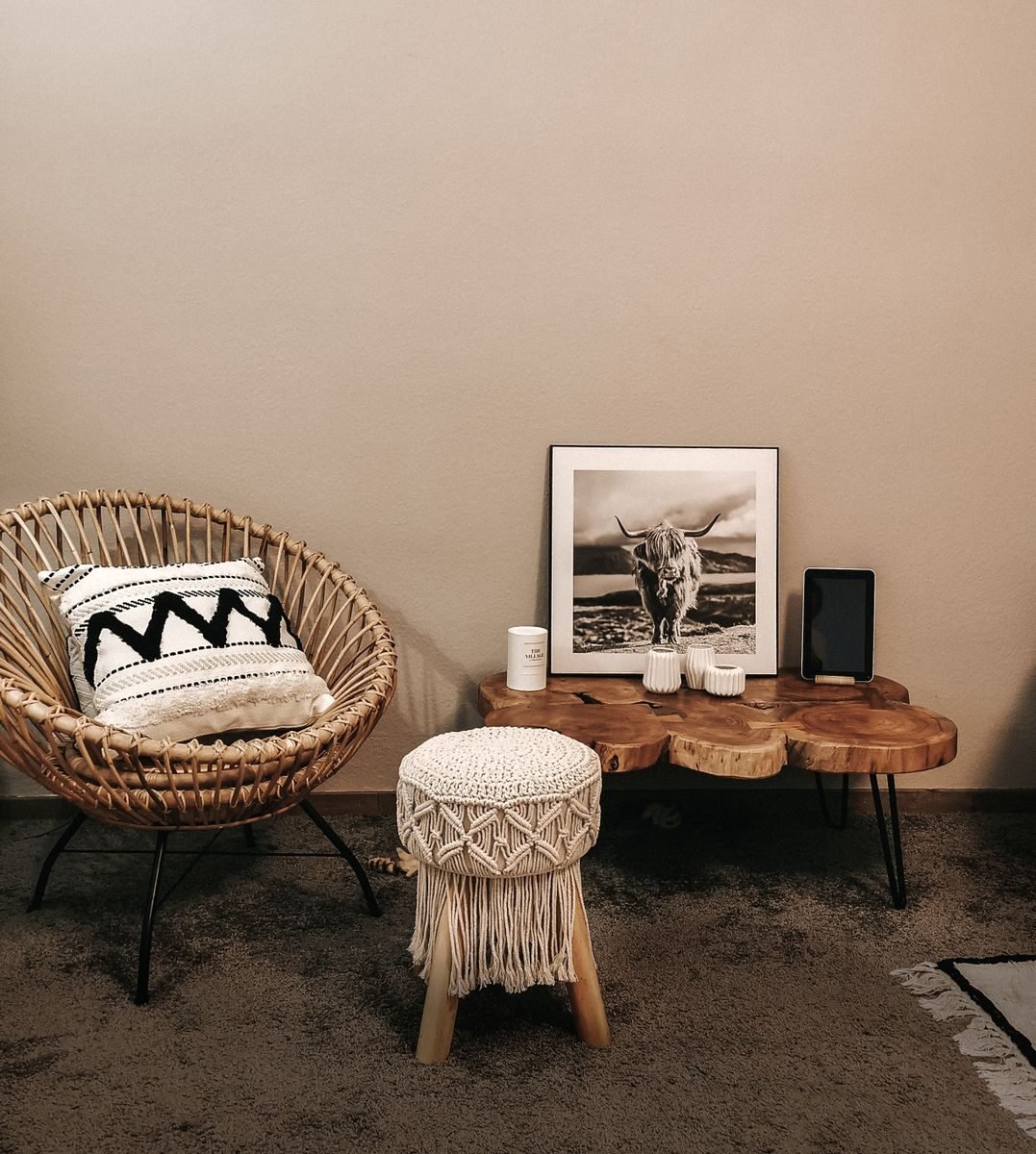 Bohemian living room with a woven wicker armchair, a macrame stool and layered textiles against a pale wall