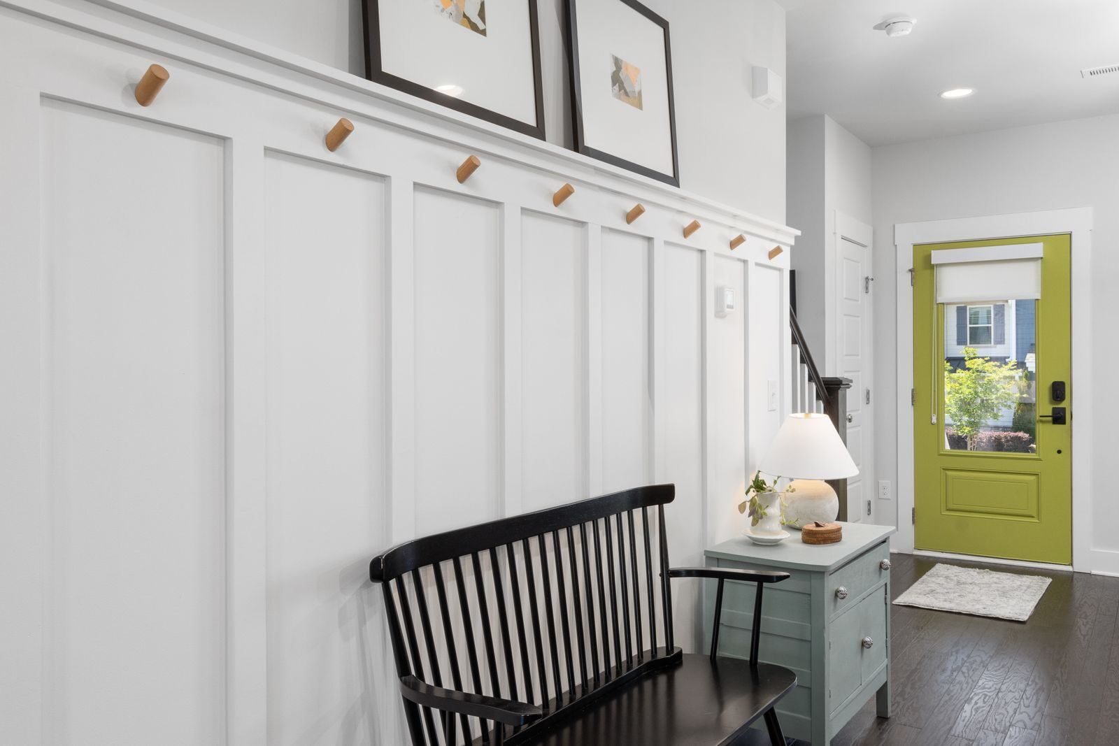 Entryway with a painted green door, a black bench for putting shoes on and baskets stored underneath it