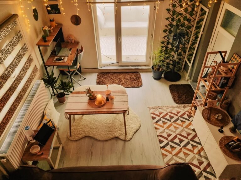 A wooden desk built into the corner of a warmly lit living room, with indoor plants and a lamp at eye level