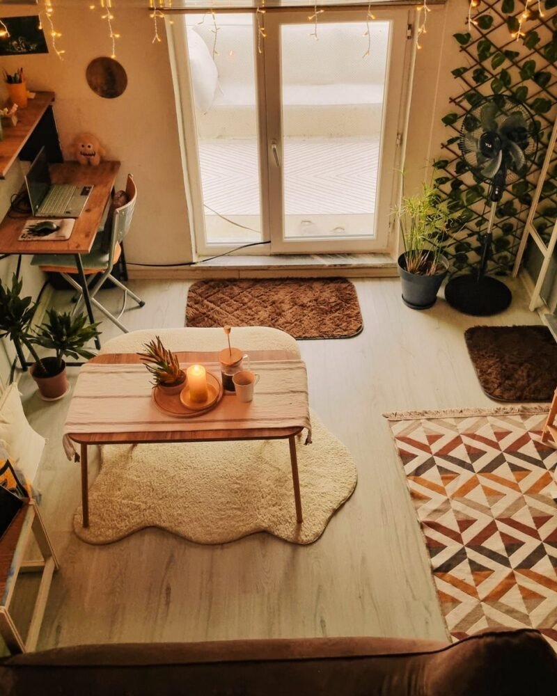A wooden desk built into the corner of a warmly lit living room, with indoor plants and a lamp at eye level