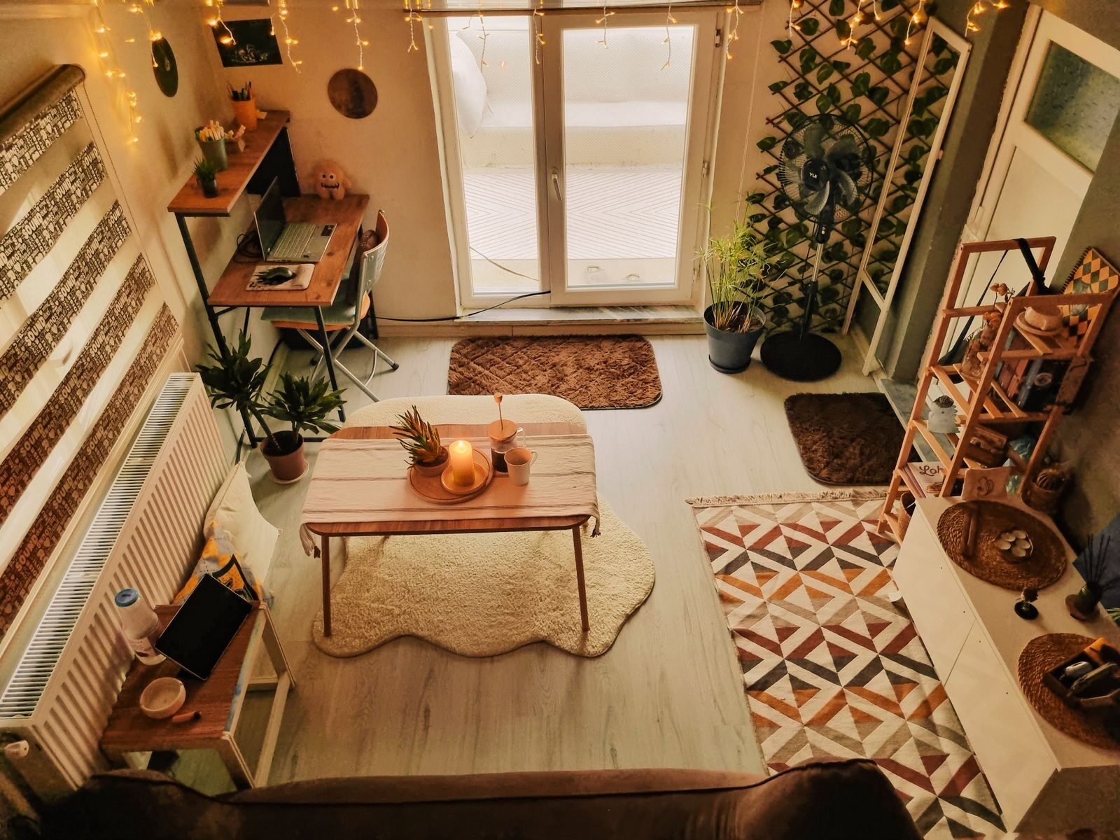 A wooden desk built into the corner of a warmly lit living room, with indoor plants and a lamp at eye level