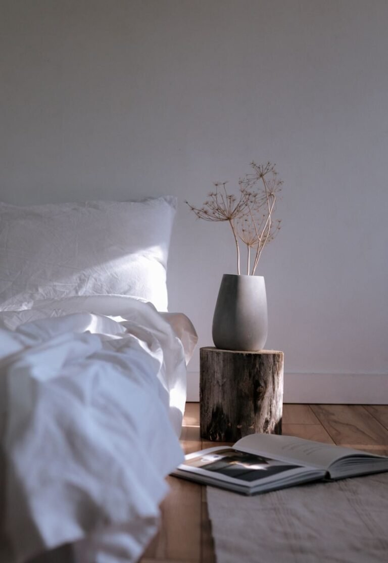 Japandi bedroom with a low wooden bed frame, oatmeal linen bedding and a single branch in a ceramic vase