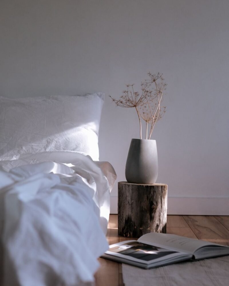 Japandi bedroom with a low wooden bed frame, oatmeal linen bedding and a single branch in a ceramic vase