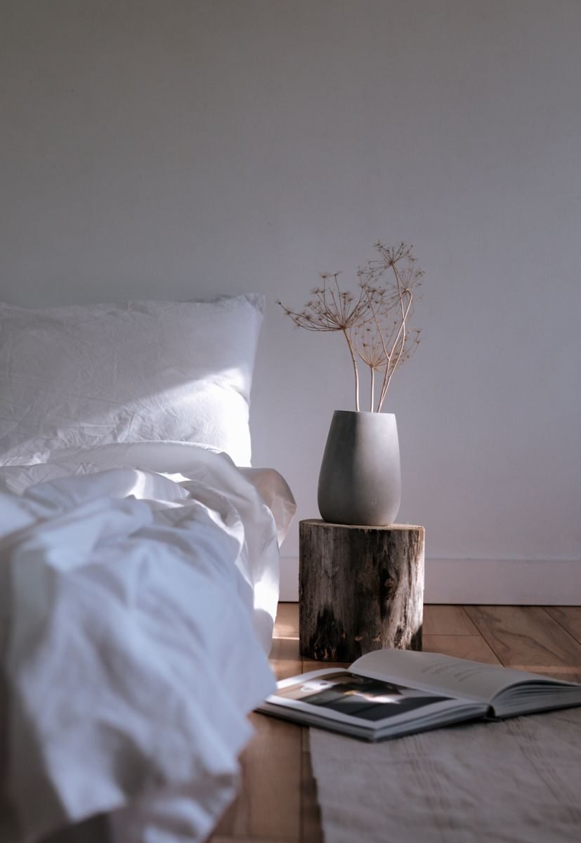 Japandi bedroom with a low wooden bed frame, oatmeal linen bedding and a single branch in a ceramic vase