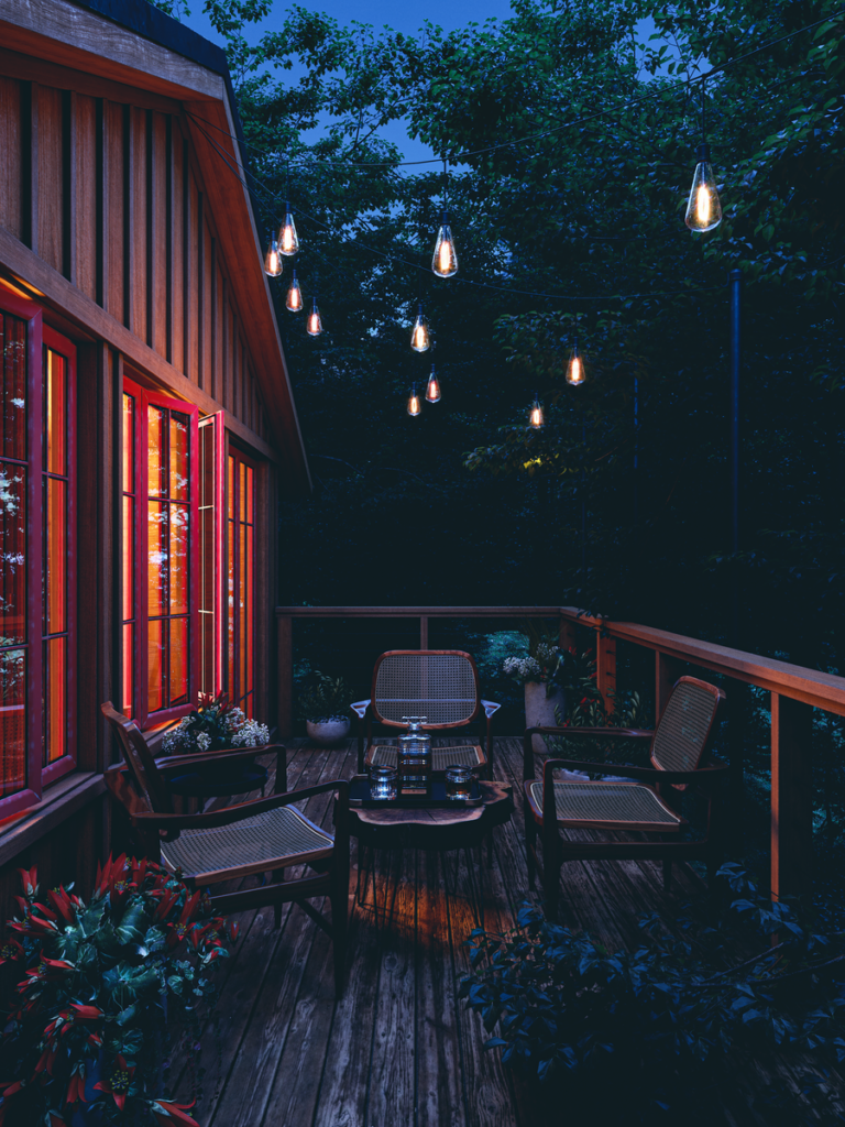 Outdoor seating area on a wooden deck lit by string lights strung overhead at twilight