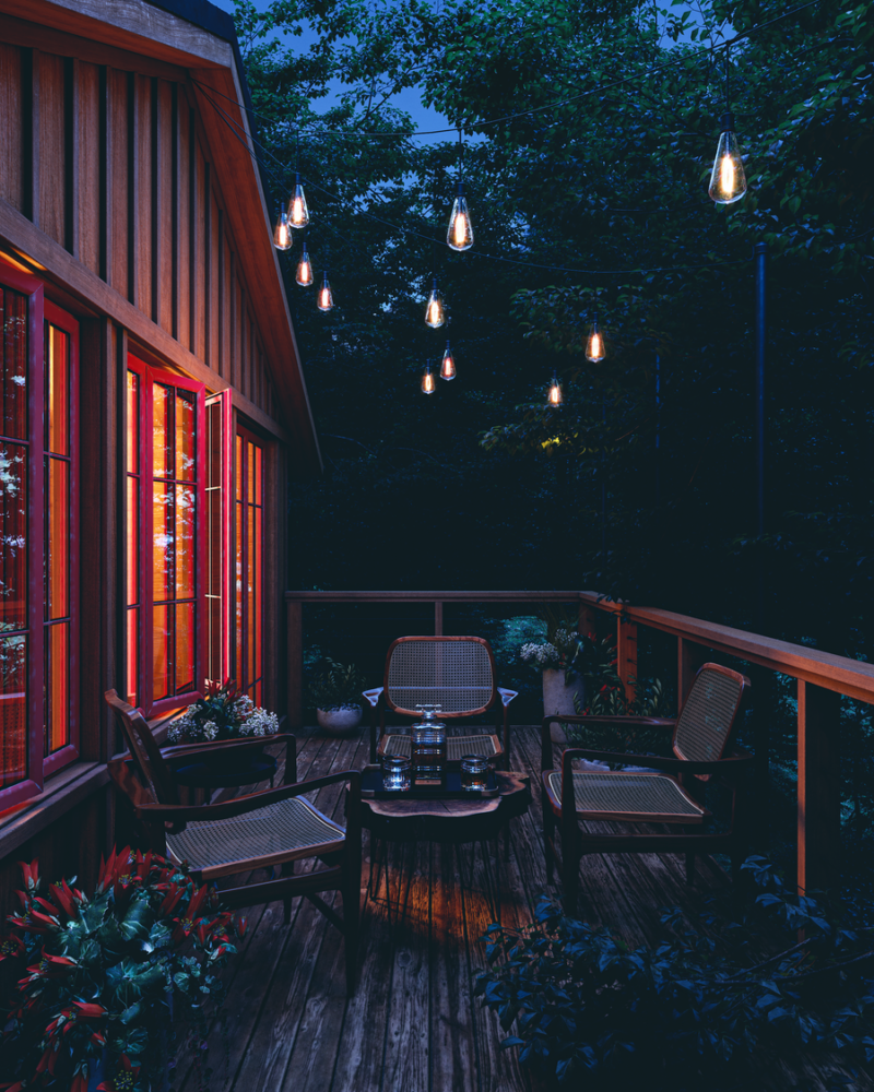 Outdoor seating area on a wooden deck lit by string lights strung overhead at twilight